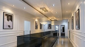 A modern hallway with a glass railing, recessed lighting, and framed pictures on the walls.