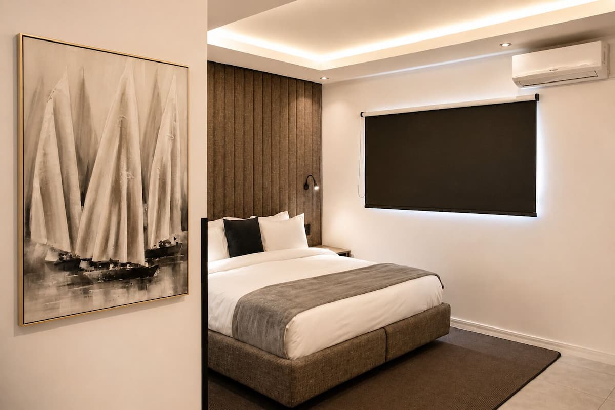 A modern bedroom with a bed, a mounted air conditioner, a large window with blackout curtains, and a framed painting.