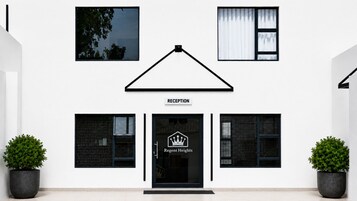 Un edificio con área de recepción, ventanas con marco negro y dos plantas en macetas.