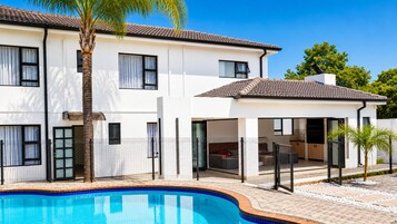 Una casa moderna de dos pisos con piscina, ventanas grandes y un patio cubierto.