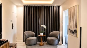 A modern living room with two grey armchairs, a small wooden side table with a white vase, and a large window with dark curtains. - Regent Heights Hotel (Ruiterhof, Sandton)