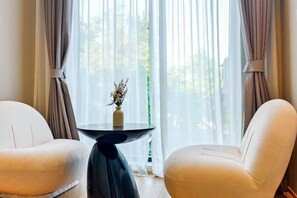 Ein Zimmer mit zwei weißen Stühlen, einem runden Tisch mit einer Vase und durchsichtigen Vorhängen.
