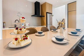 Eine moderne Küche mit einem dreistöckigen Kuchenbuffet, einer eingebauten Dunstabzugshaube und einem Essbereich mit einem langen Tisch, gedeckt für eine Mahlzeit.