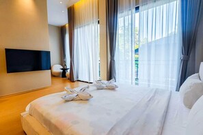 Ein Hotelzimmer mit einem großen Bett, einem flachbildfernseher an der Wand und Blick auf Grünfläche.