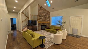 Un salon spacieux avec une cheminée en pierre, un escalier en bois et un grand téléviseur.