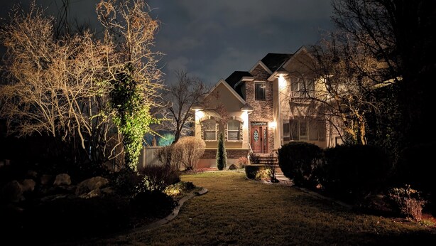 A two-story house with a stone facade, a front porch, and a well-lit entrance. - River House - Entire 6-bedroom, 3.5 bathroom home near the SF River trail (Spanish Fork)