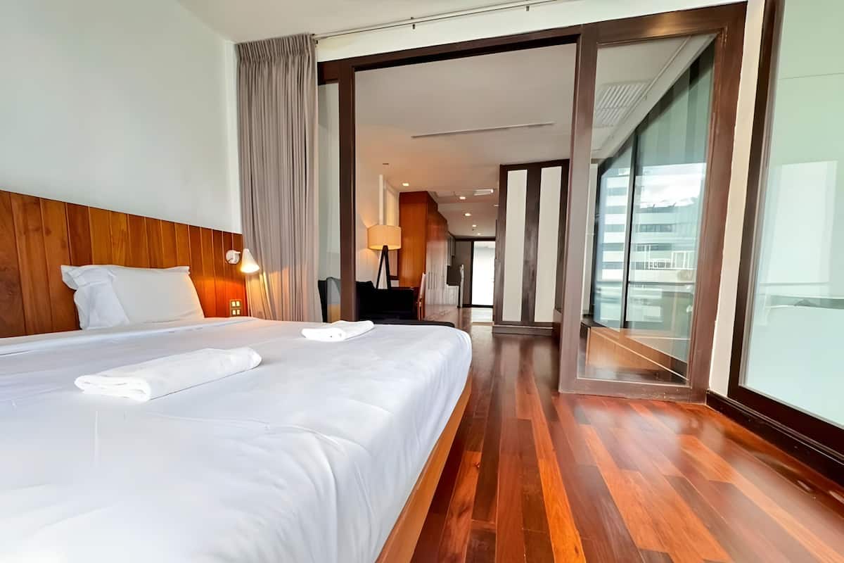 Une chambre d’hôtel avec un grand lit, une tête de lit en bois et une vue sur l’extérieur, visible à travers une porte vitrée.