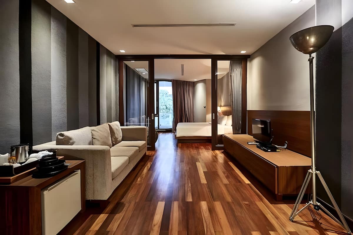 Une chambre d’hôtel moderne avec un plancher en bois, un canapé, un bureau avec une télévision et une grande fenêtre.