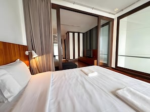 A hotel room with a bed, a TV, a desk, and a large window.