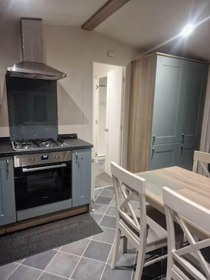 A kitchen with a stove, oven, and cabinets. There is a dining table with chairs. - Marine Holiday Park - Holiday Accommodation 16604 (Rhyl)