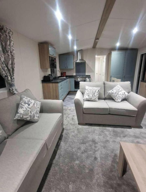 A modern living room with a sofa, a coffee table, and a kitchen area in the background. - Marine Holiday Park - Holiday Accommodation 16604 (Rhyl)