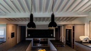 Une cuisine moderne dotée d’un îlot central, de luminaires suspendus noirs, d’appareils électroménagers en acier inoxydable et d’un panier à fruits.