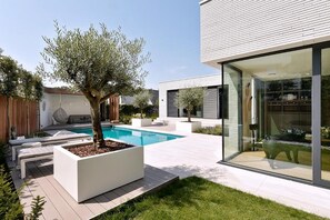 Una casa moderna con piscina, mobiliario exterior y un amplio ventanal.