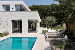 Ein modernes Haus mit Schwimmbad, Terrassenmöbeln und Garten.
