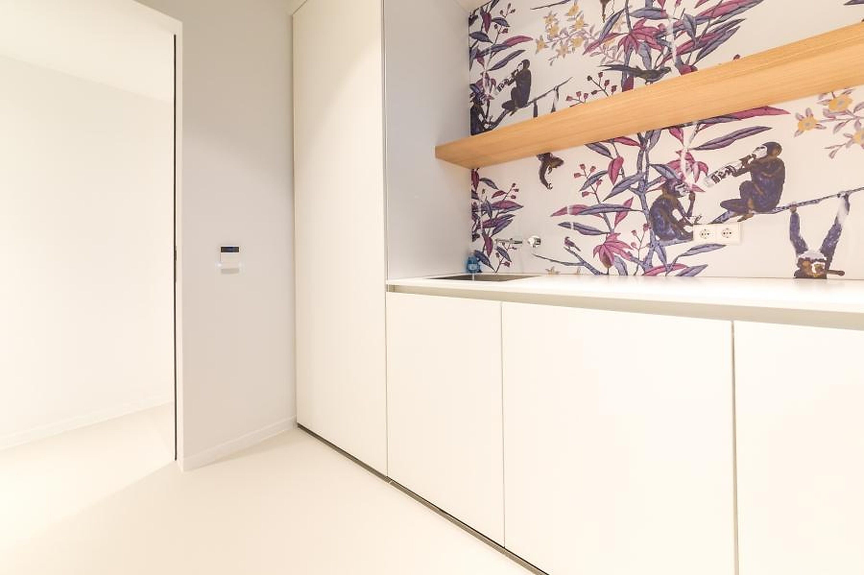 A modern kitchen with white cabinetry, a wooden shelf, and a floral backsplash.