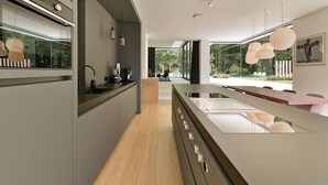 A modern kitchen with a central island, a dining area with a long table, and large windows offering a view of greenery. - Exclusive family villa with pool, jacuzzi and 3 luxury suites in Brabant (Goirle)