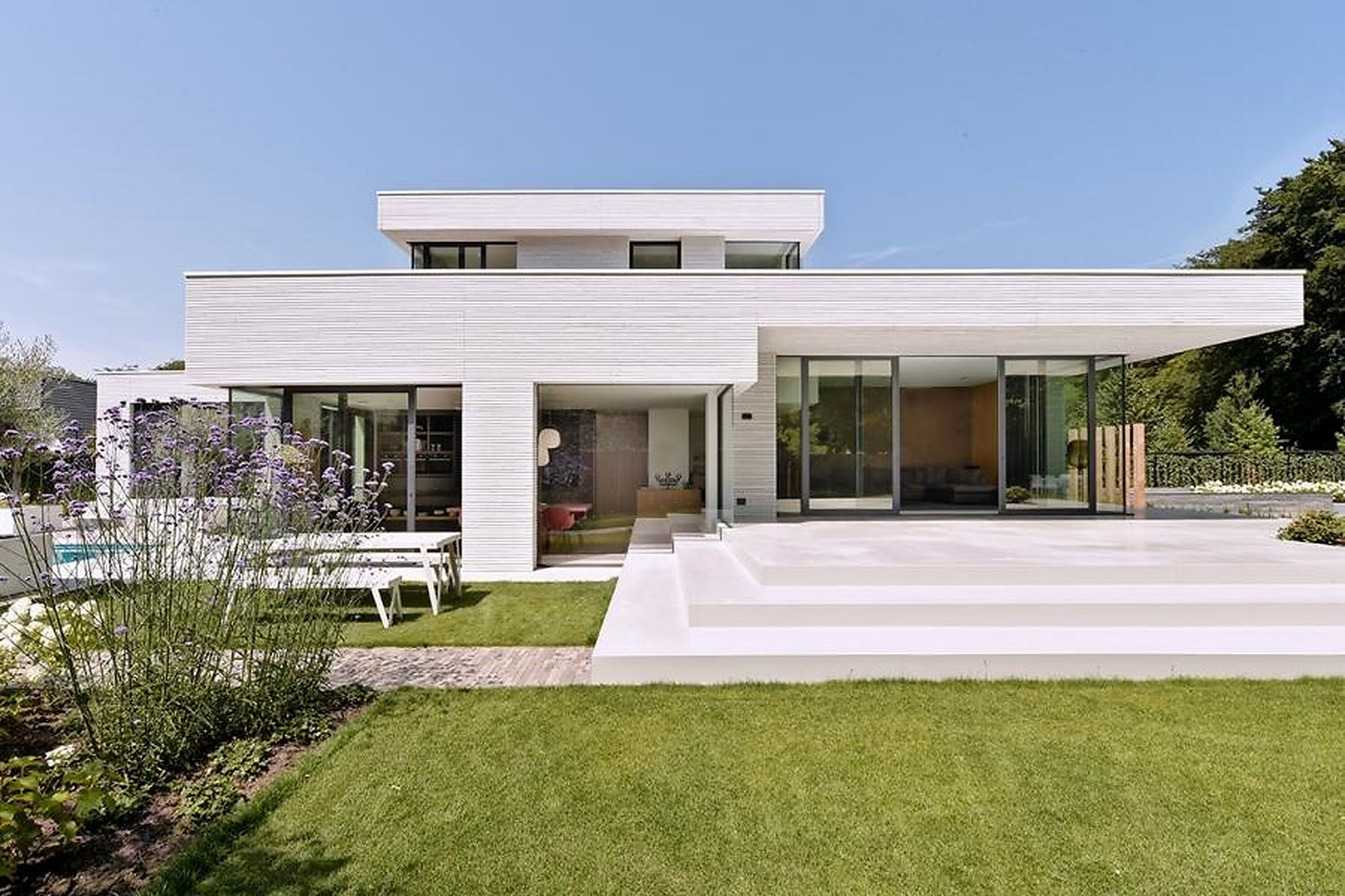 Et moderne hus i to etager med fladt tag, store glasruder og en velplejet græsplæne.