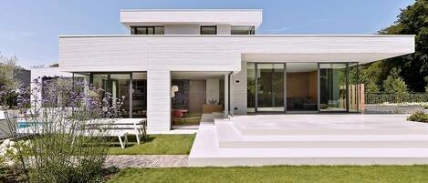 Et moderne hus i to etager med fladt tag, store glasruder og en velplejet græsplæne.