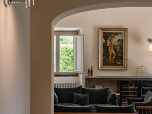 A living room with a green sofa, a painting of a woman holding a flower, a radiator, and a wine cooler. - L'Orto di Vignamaggio (Greve in Chianti)