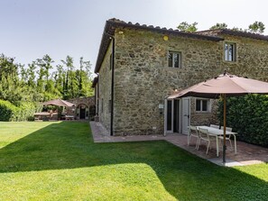 A stone building with a patio area, outdoor seating, and a well-maintained lawn. - L'Orto di Vignamaggio (Greve in Chianti)
