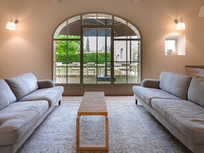 A room with two sofas, a wooden bench, and a large arched window with a view of an outdoor patio. - L'Orto di Vignamaggio (Greve in Chianti)
