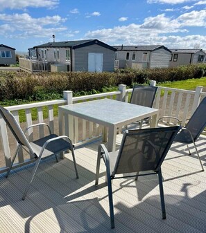 Eine Terrasse mit Tisch und Stühlen, ein weißer Zaun und Mobilheime im Hintergrund.