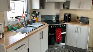A compact kitchen with a sink, stove, and cabinets. - Primrose Valley Holiday Park - Holiday Accommodation 1421 (Filey)