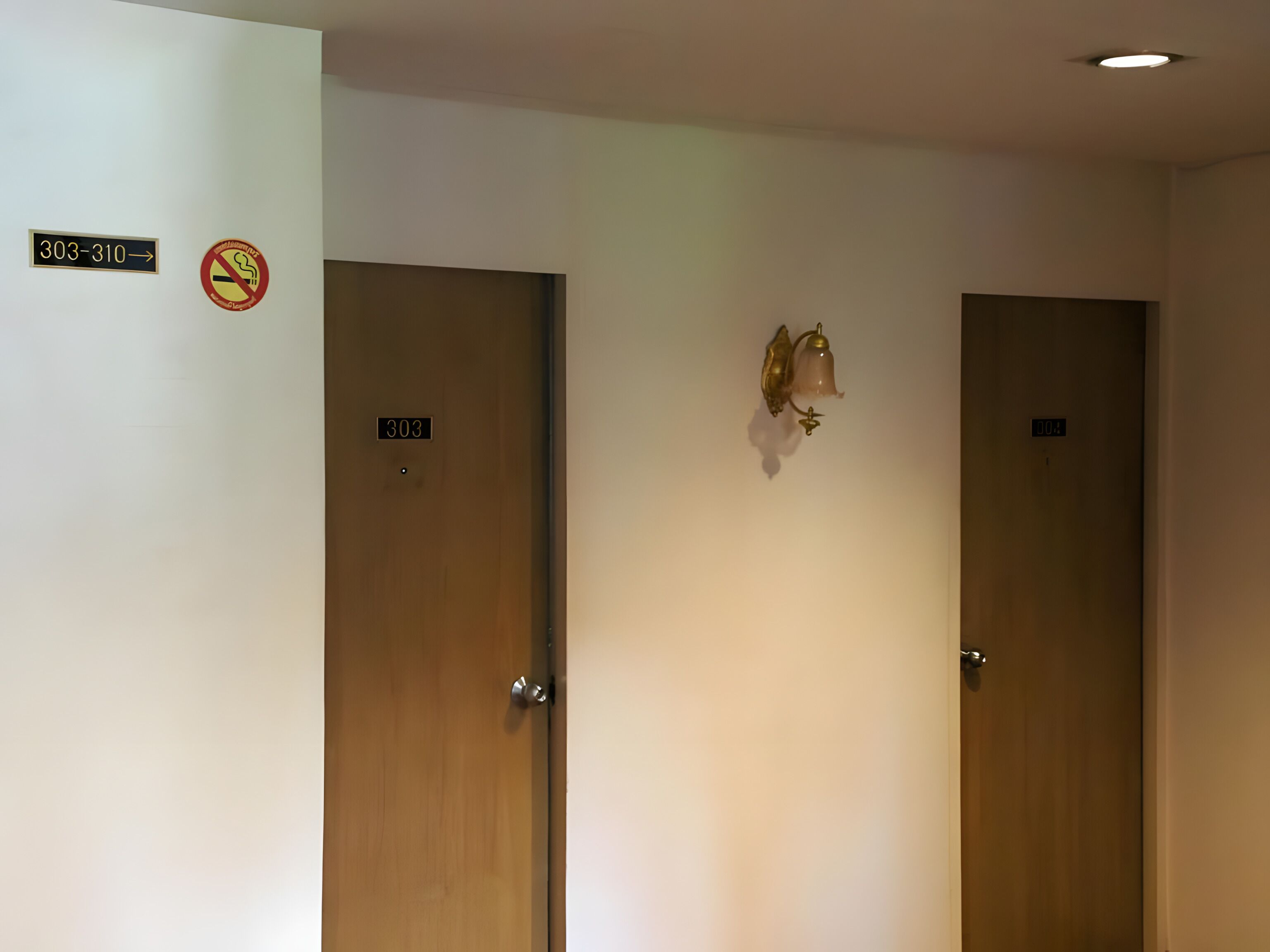 Two wooden doors with room numbers 303 and 310, a no-smoking sign, and a wall-mounted light fixture.