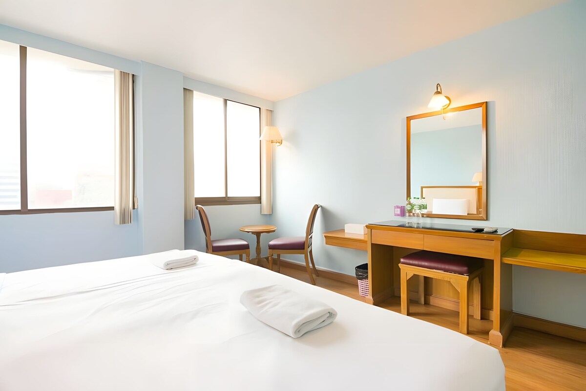 Habitación de hotel con cama, escritorio, silla, mesita y espejo.