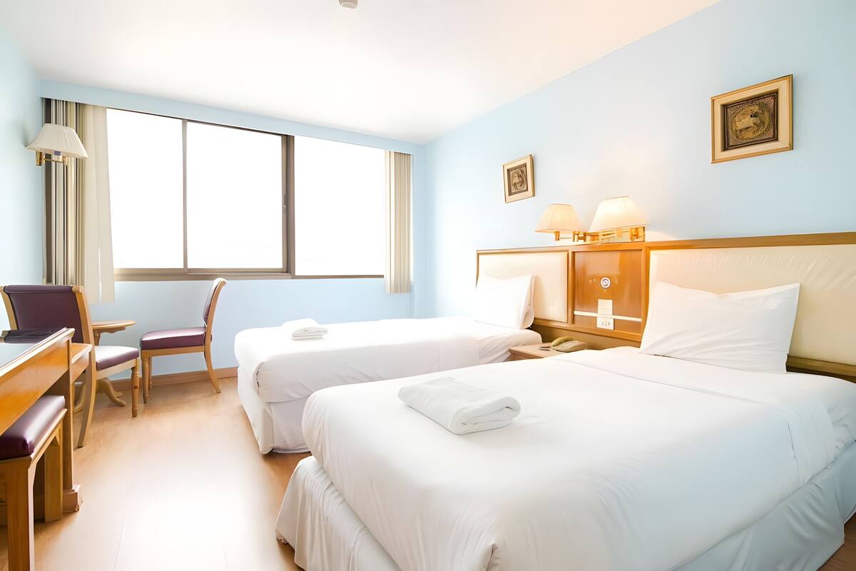 A hotel room with two beds, a desk, a chair, and a window.