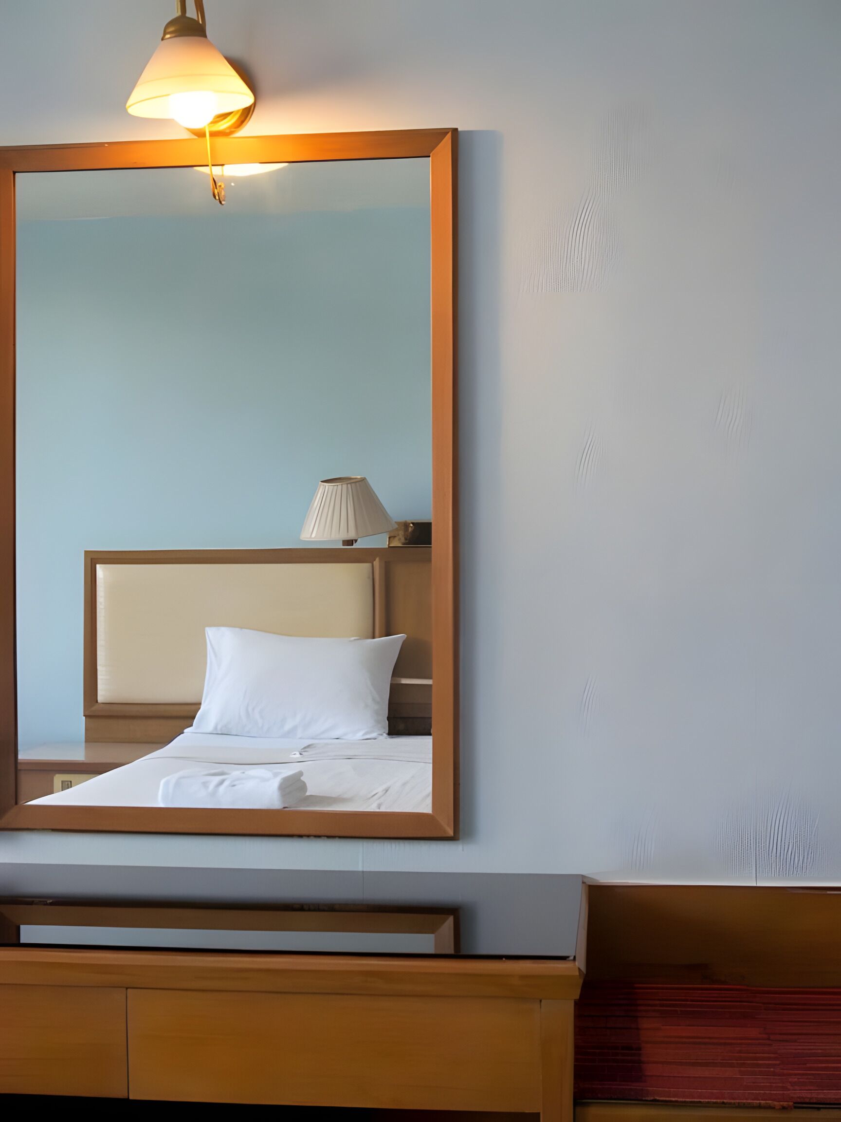 A hotel room with a bed, a nightstand, a lamp, and a large mirror.