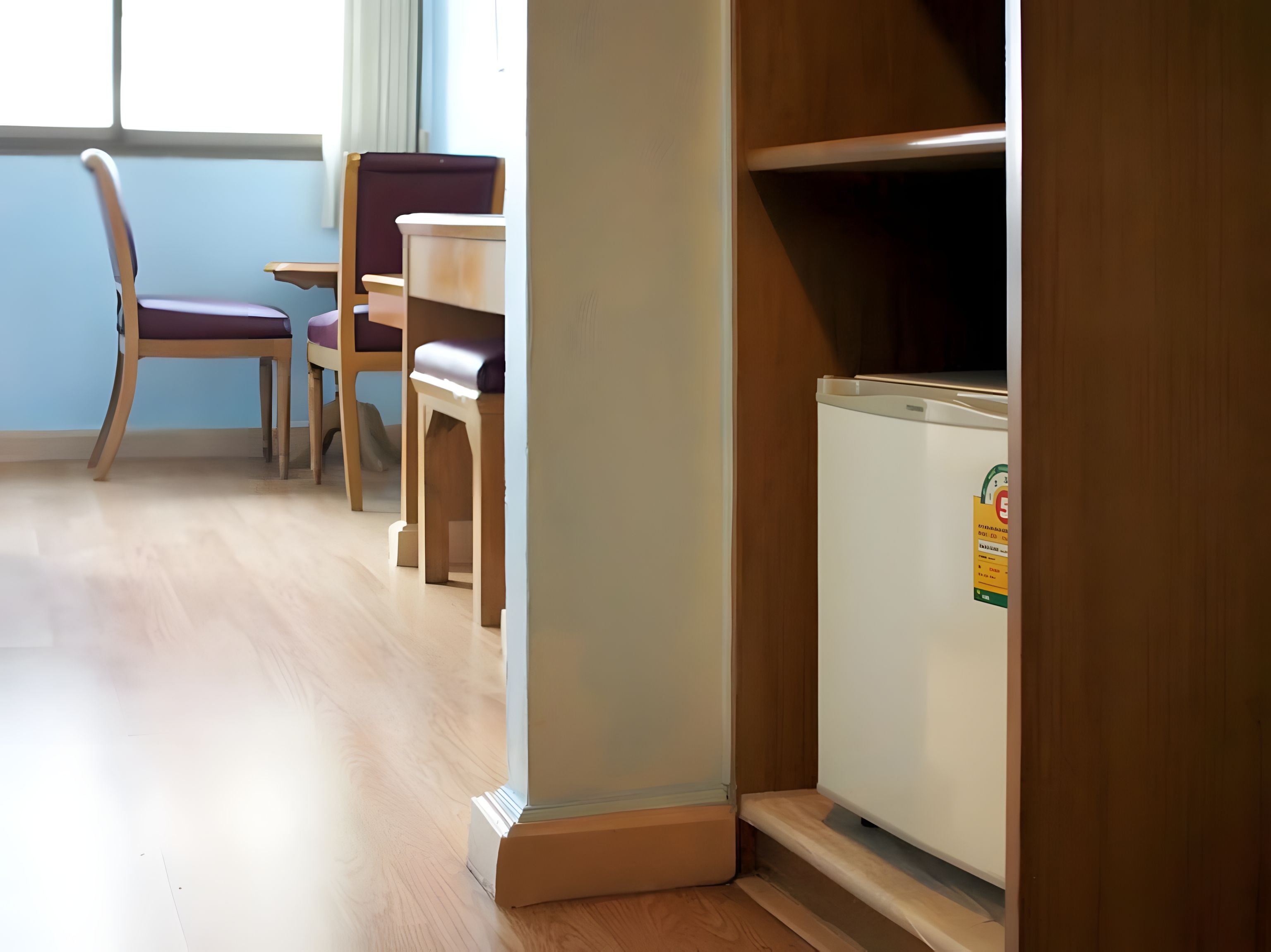 Una habitación con piso de madera, un refrigerador blanco, una silla de madera y una mesa.