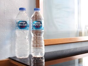 Dos botellas de agua Nestlé Pure Life sobre una superficie reflectante cerca de una ventana con pared texturizada.