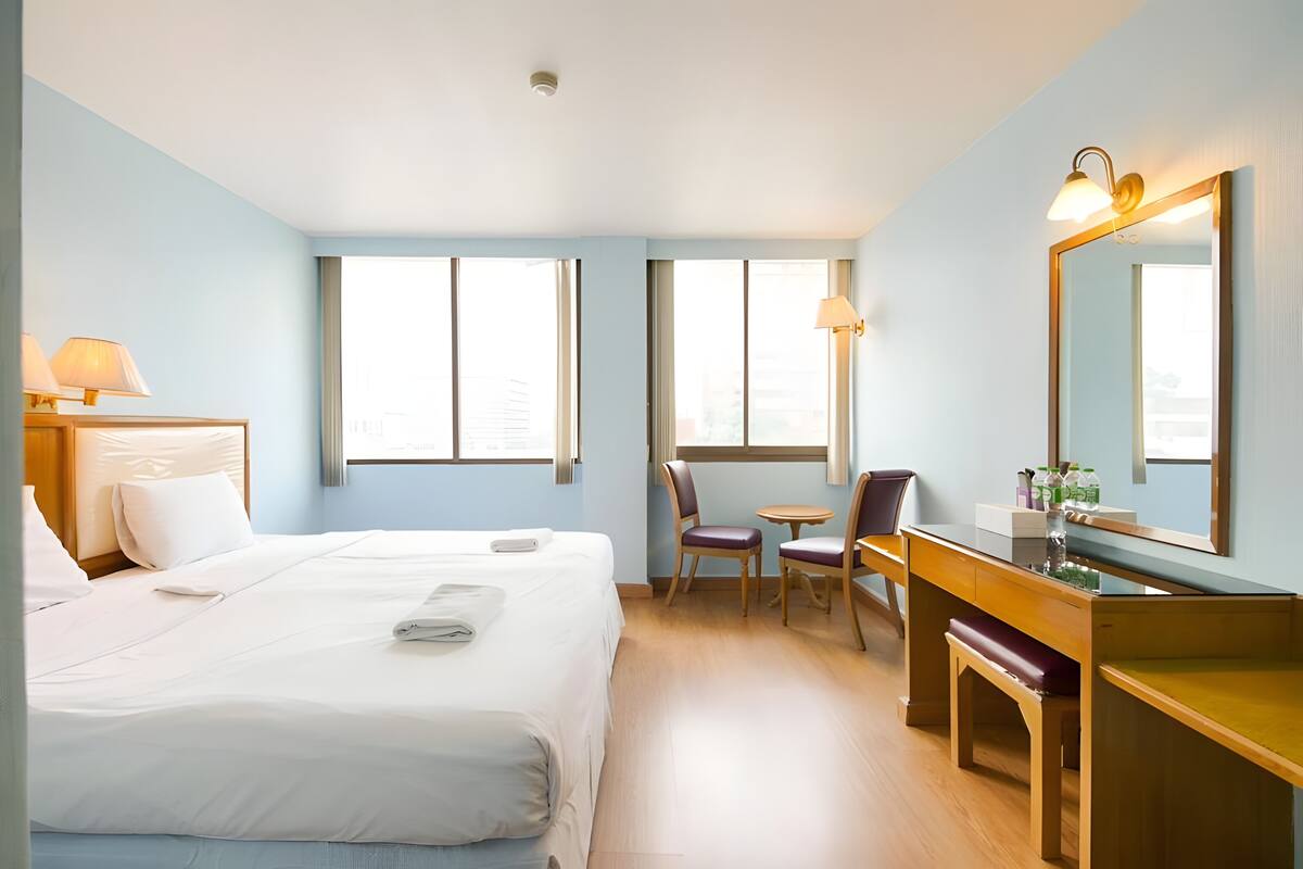 A hotel room with a bed, a desk, a chair, a mirror, and windows.