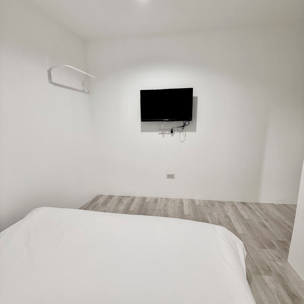 Una habitación de hotel minimalista con cama, televisor montado y suelo de madera.
