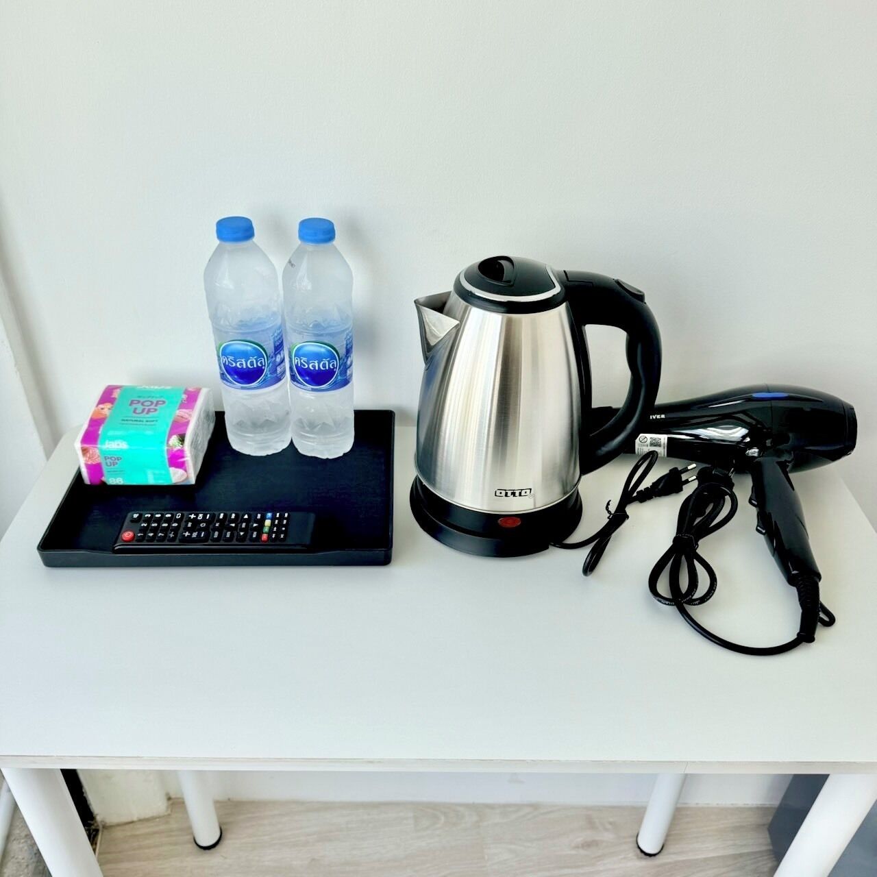 A small table with a kettle, two water bottles, a box of tissues, and a remote control.