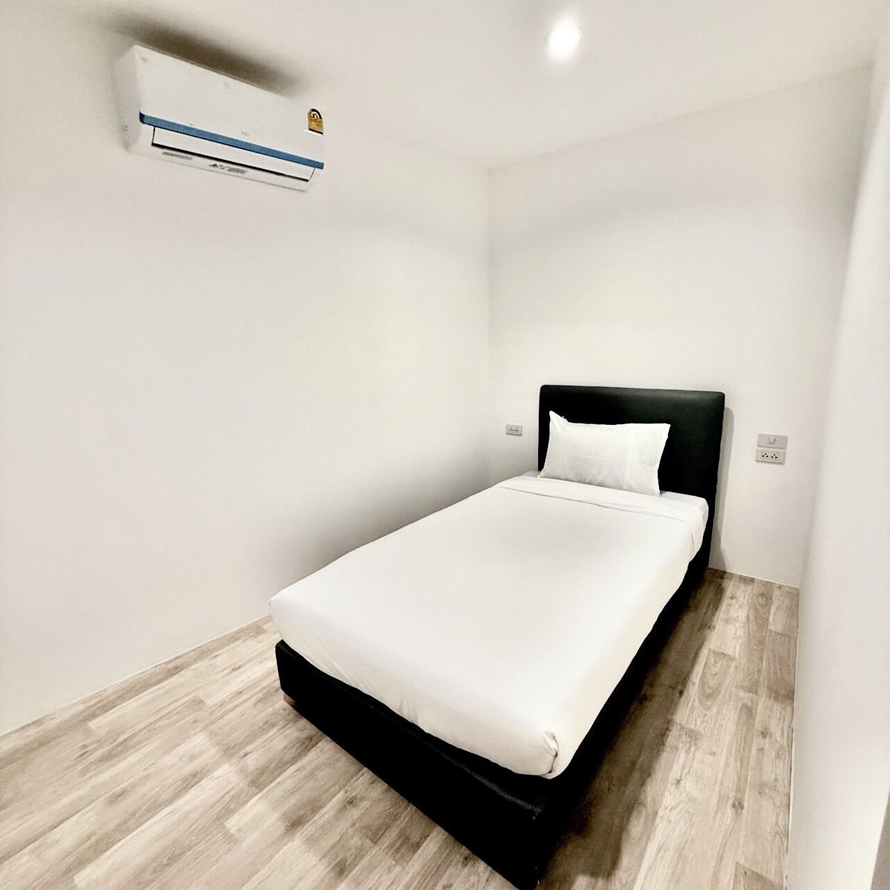 A single bed with a black headboard in a room with white walls and a wooden floor.