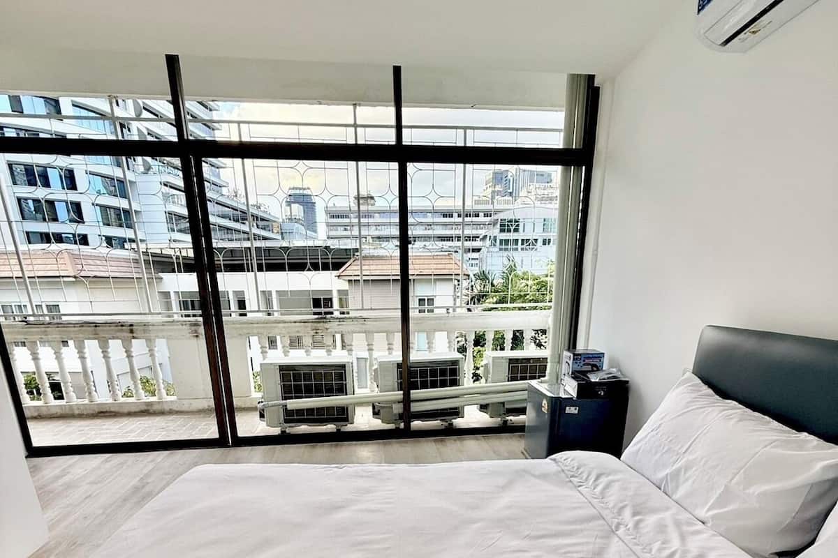 Habitación de hotel moderna con una cama grande, una mesita de noche y vistas de la ciudad a través de ventanales de piso a techo.