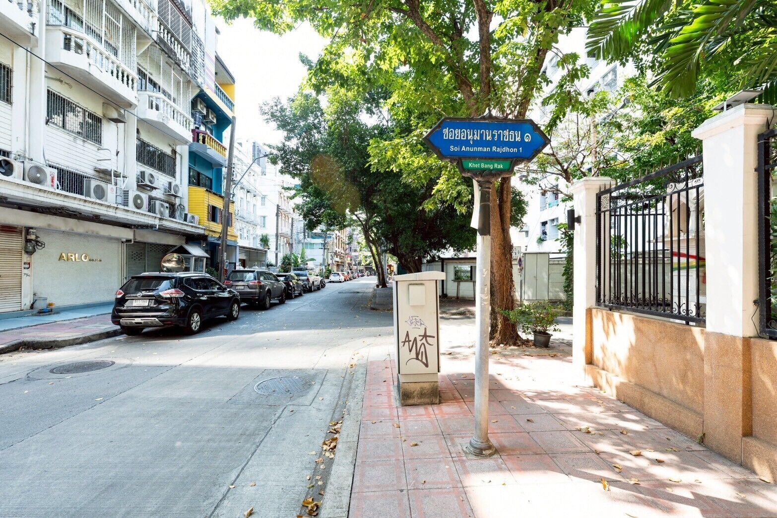 A street with parked cars, a blue directional sign, and a building with balconies.
