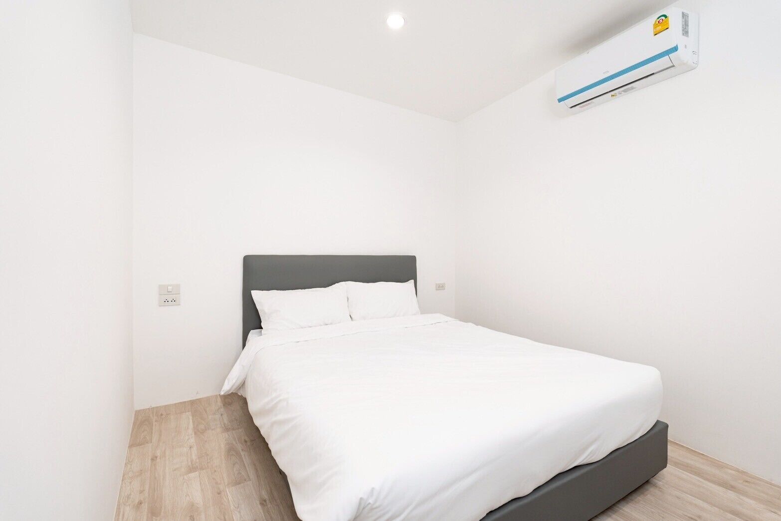 A clean, modern hotel room with a single bed, a gray headboard, and a white wall.