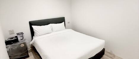 Ein kleines, sauberes Zimmer mit einem Einzelbett, einem Nachttisch, einem Mülleimer und einer Wand-Klimaanlage.