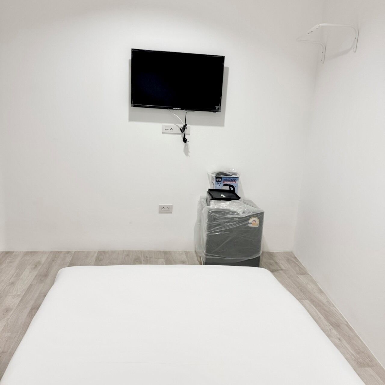 A room with a bed, a television mounted on the wall, and a small desk with a computer and a bag of toiletries.