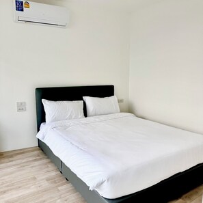 Ein Einzelbett mit weißer Bettwäsche, einem schwarzen Kopfteil und einer Wand-Klimaanlage.