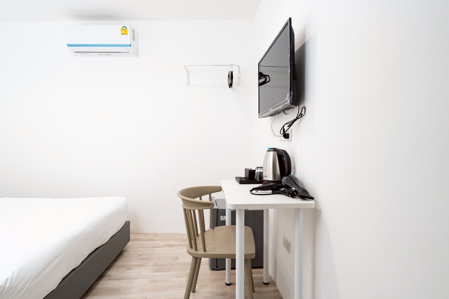 A hotel room with a bed, a desk with a chair, a TV, and an air conditioning unit.