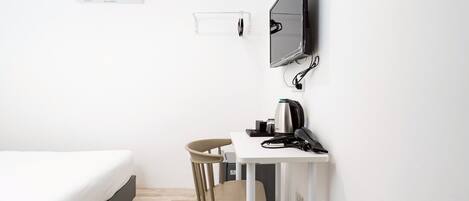 A hotel room with a bed, a desk with a chair, a TV, and an air conditioning unit.