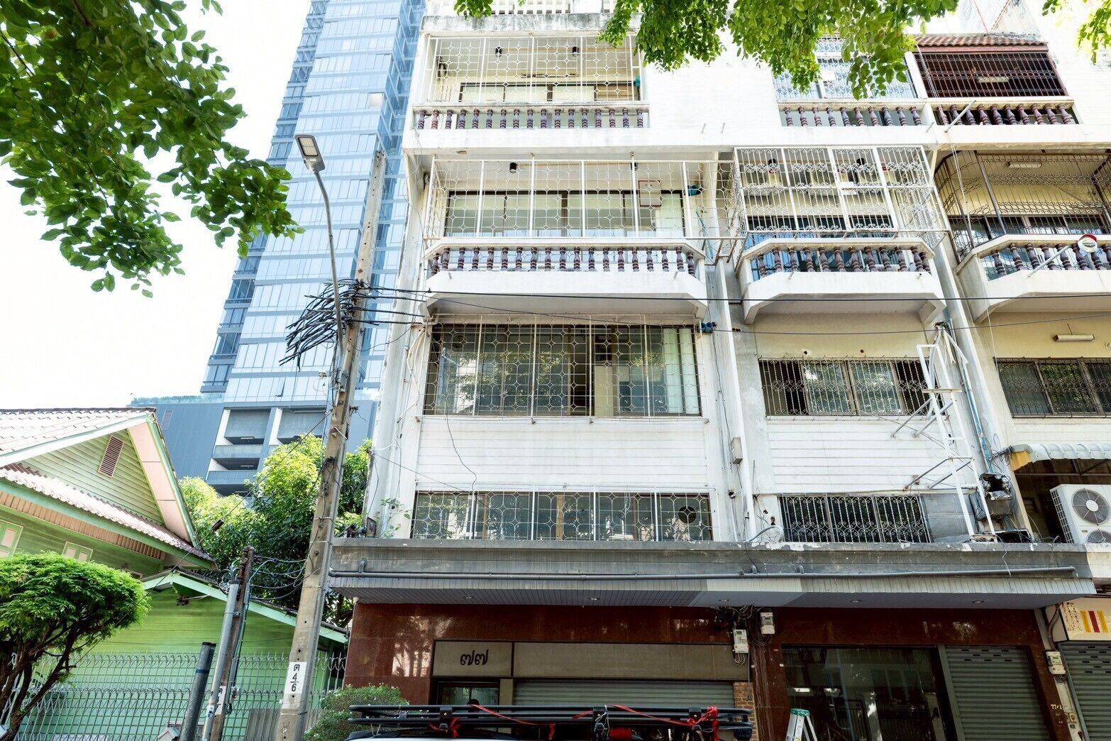 A multi-story building with balconies, a storefront at the ground level, and a neighboring high-rise building.