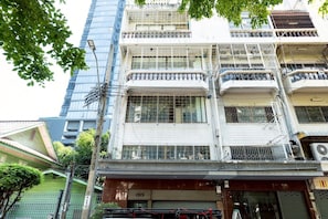 A multi-story building with balconies, a storefront at the ground level, and a neighboring high-rise building.