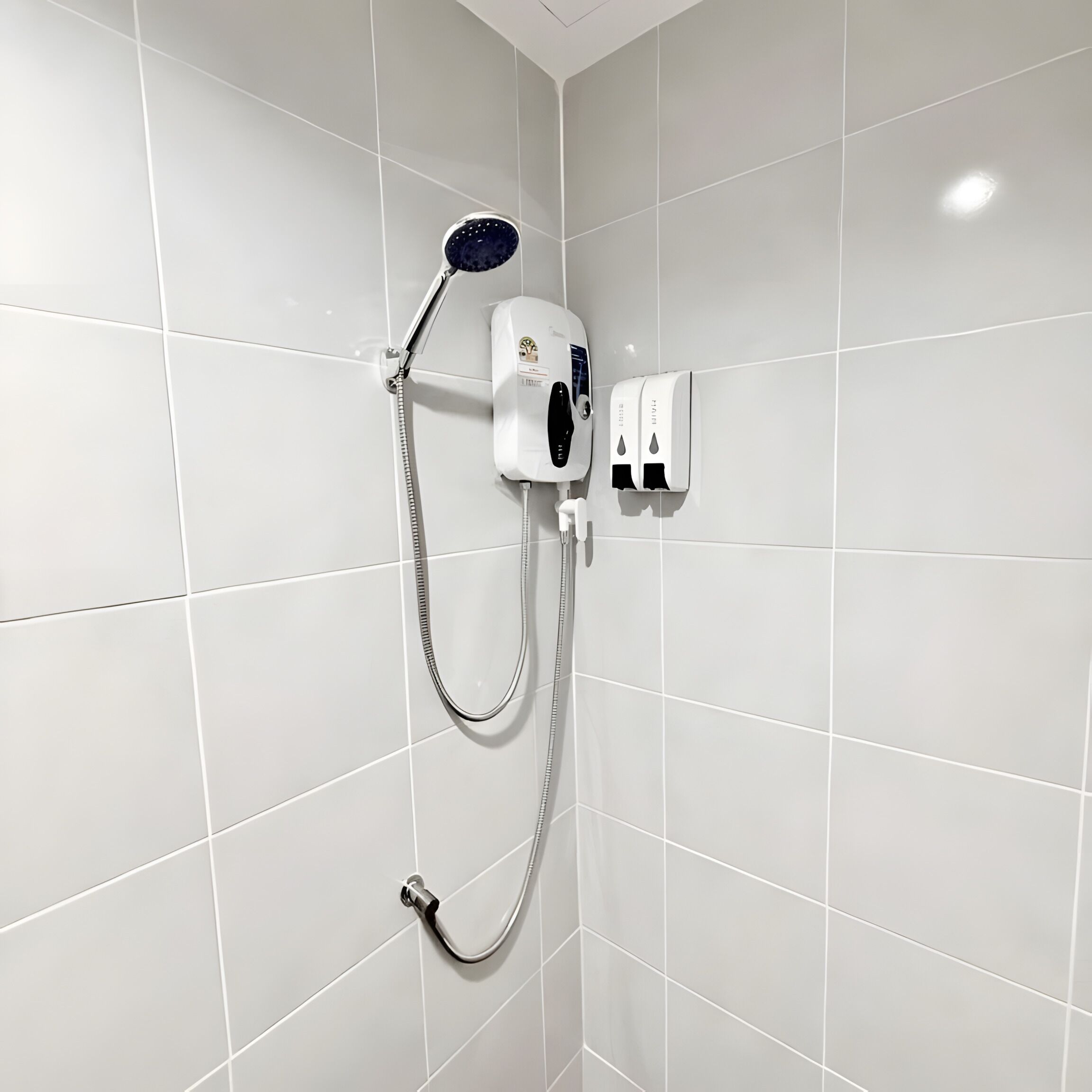 Eine Dusche mit Duschbrause, Seifenspender an der Wand und Duschschlauch.