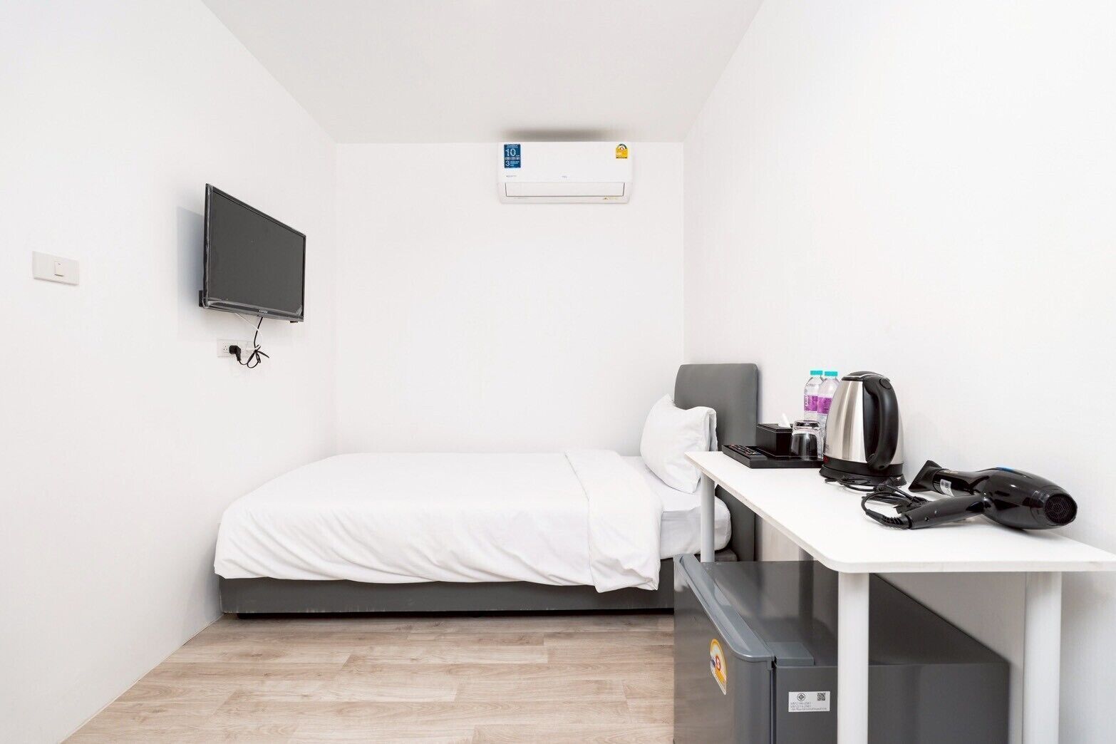 Une petite chambre propre, équipée d’un lit, d’un bureau avec une bouilloire, d’un sèche-cheveux et d’une poubelle.