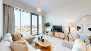 A modern living room with a sofa, TV, and lamp, large windows with curtains, and a city view. - Mesmerizing 2 Bed l Canal and Burj Views (Al Wasl)